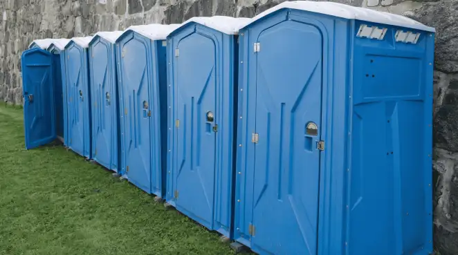 Row of blue portable toilets lined up on grass against a stone wall for event sanitation in Bradenton, FL