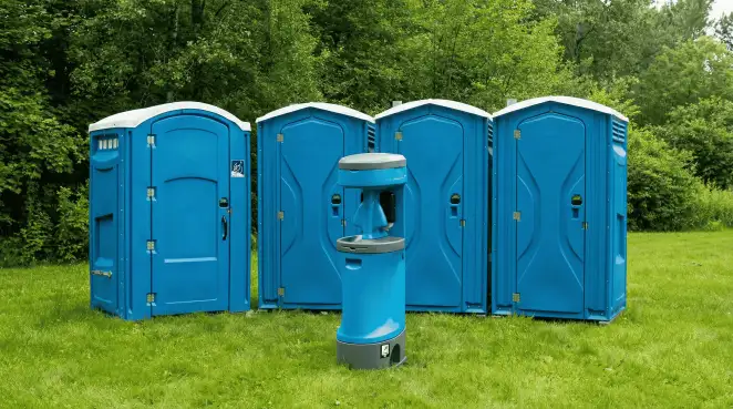 Four blue portable toilets and a matching hand washing station on grass near trees, a common sight at local outdoor events in Bradenton, FL